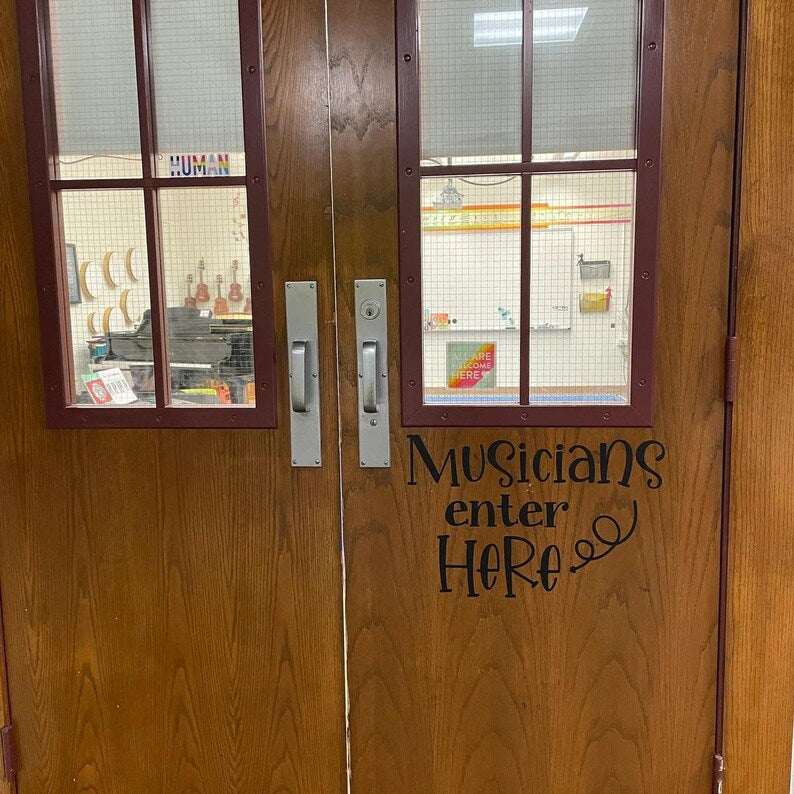 Musicians Enter Here decal on double wooden classroom doors with glass panels and musical instruments visible inside
